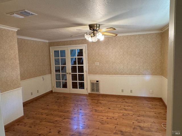 empty room with wood finished floors, visible vents, french doors, wainscoting, and wallpapered walls