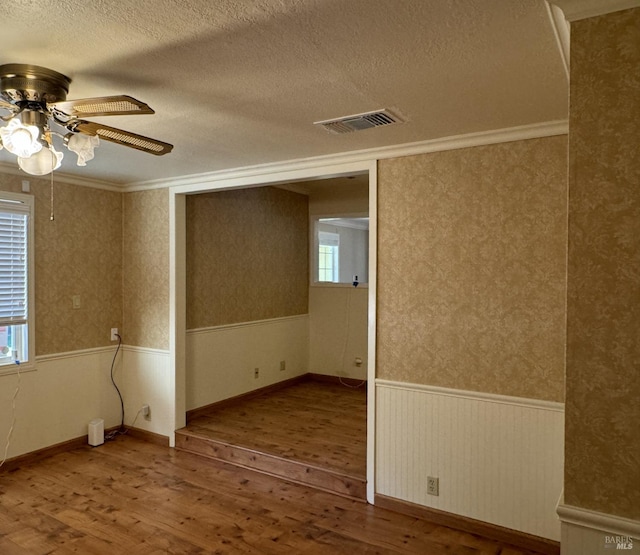 spare room featuring hardwood / wood-style flooring, wainscoting, visible vents, and wallpapered walls