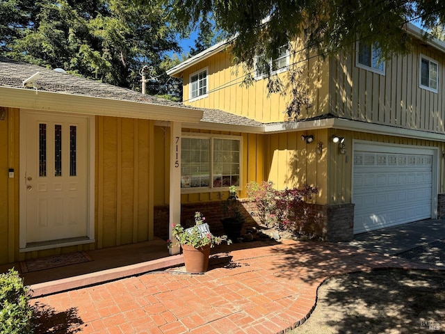 doorway to property featuring board and batten siding, roof with shingles, and a garage