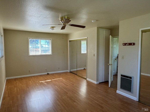 unfurnished bedroom featuring heating unit, ceiling fan, a textured ceiling, wood finished floors, and baseboards