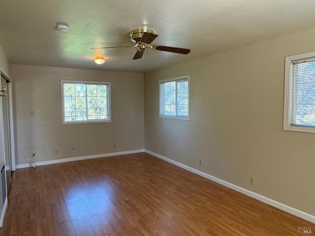 unfurnished bedroom featuring ceiling fan, a textured ceiling, baseboards, and wood finished floors