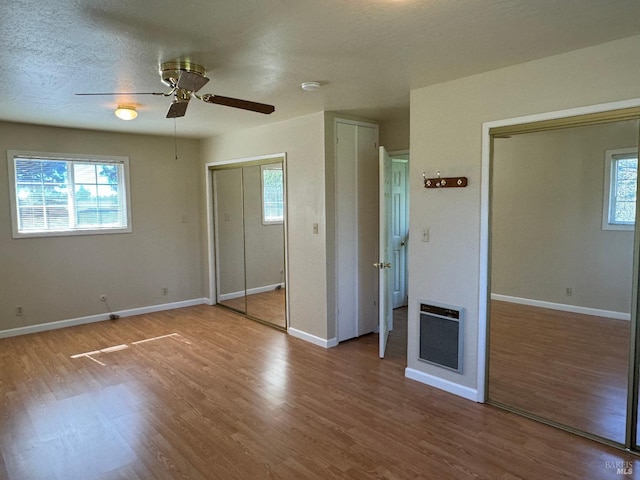 unfurnished bedroom featuring heating unit, multiple closets, baseboards, and wood finished floors