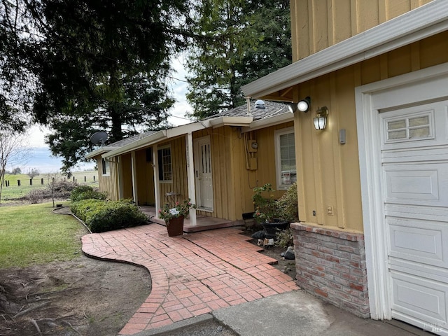 doorway to property with an attached garage, board and batten siding, and a yard