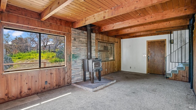 unfurnished living room featuring stairs, beamed ceiling, wooden walls, and a wood stove