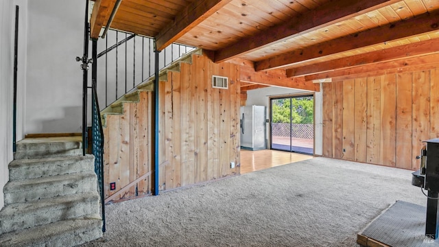 unfurnished living room featuring stairs, beam ceiling, wood walls, and carpet flooring