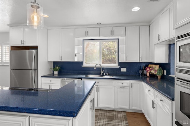 kitchen with stainless steel appliances, dark countertops, white cabinets, and a sink