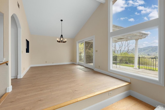 unfurnished dining area with a notable chandelier, high vaulted ceiling, a mountain view, and light wood-style floors