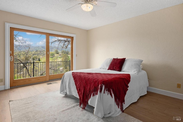 bedroom featuring a textured ceiling, wood finished floors, visible vents, baseboards, and access to outside