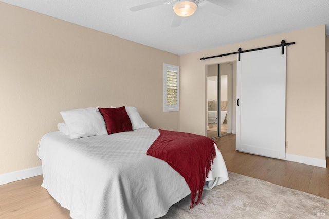 bedroom with a barn door, wood finished floors, a ceiling fan, and baseboards