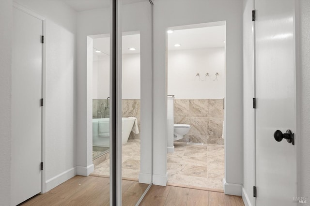 full bath featuring toilet, a freestanding bath, tile walls, and wood finished floors