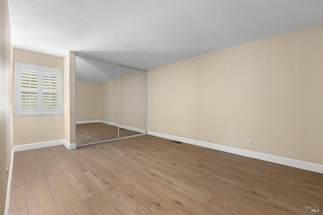 unfurnished bedroom with a closet, a textured ceiling, baseboards, and wood finished floors