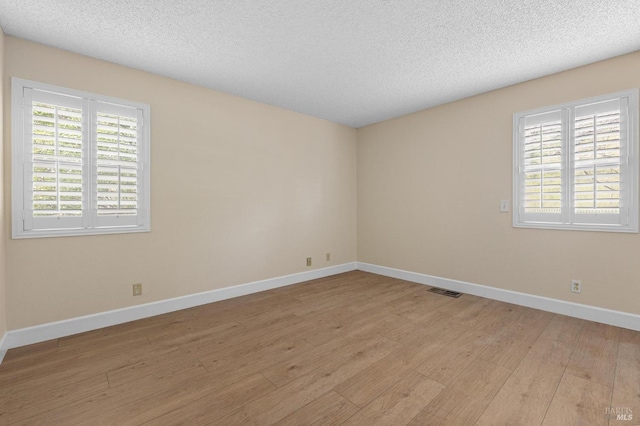 spare room with visible vents, baseboards, a textured ceiling, and light wood finished floors