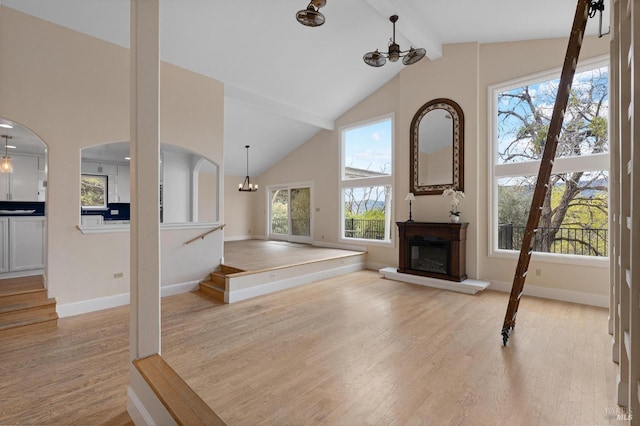 unfurnished living room with light wood-type flooring, a notable chandelier, beam ceiling, and a glass covered fireplace