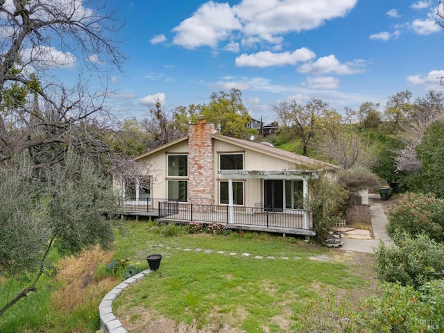 back of property with a deck, a yard, and a chimney