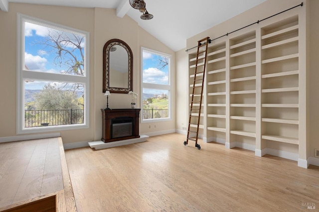 interior space featuring lofted ceiling with beams, baseboards, wood finished floors, and a glass covered fireplace