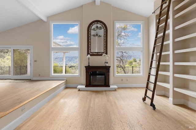 unfurnished living room featuring a glass covered fireplace, wood finished floors, beam ceiling, and baseboards