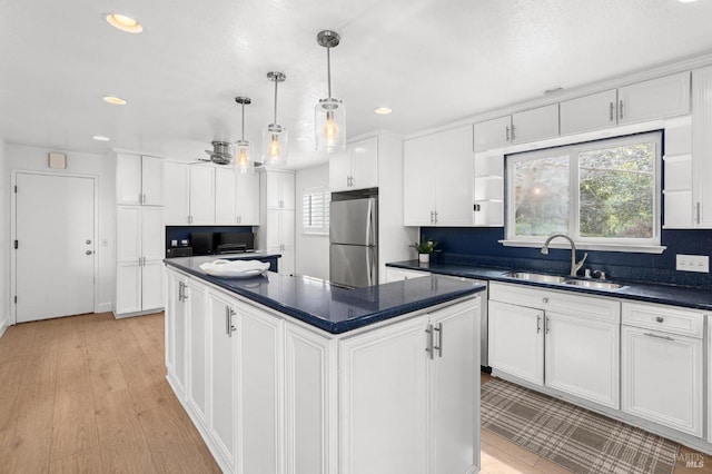 kitchen with dark countertops, white cabinets, a sink, and freestanding refrigerator