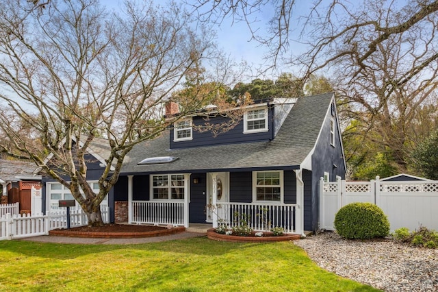 view of front of house with a chimney, roof with shingles, covered porch, fence, and a front yard