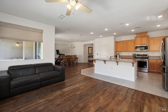 kitchen featuring visible vents, a kitchen breakfast bar, wood finished floors, open floor plan, and stainless steel appliances