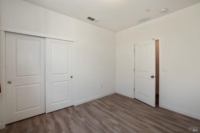 unfurnished bedroom with wood finished floors, visible vents, a closet, and baseboards