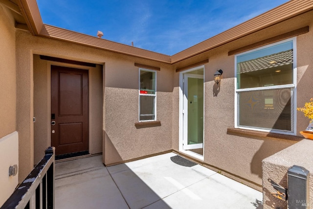 view of exterior entry featuring stucco siding and a patio