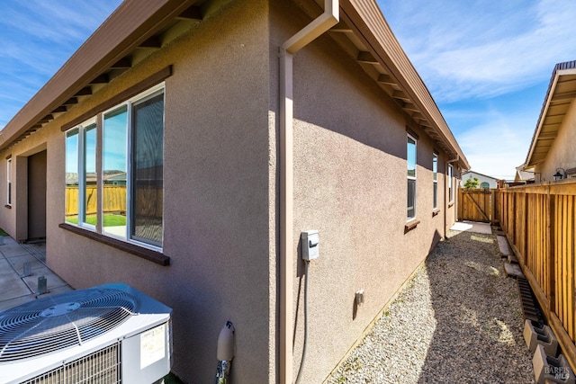 view of side of home featuring stucco siding, central AC, and a fenced backyard