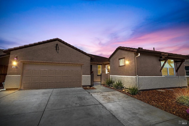 view of front of house with fence, a tiled roof, stucco siding, driveway, and an attached garage