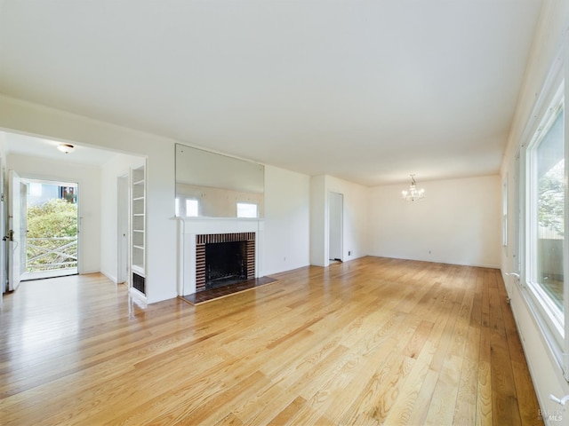 unfurnished living room with a brick fireplace, light wood-style flooring, a wealth of natural light, and a chandelier