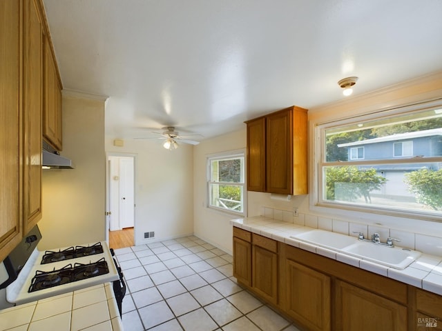 kitchen with visible vents, brown cabinets, gas stove, a ceiling fan, and a sink