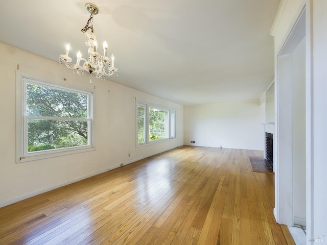 unfurnished living room featuring baseboards, a fireplace, light wood-style floors, and a chandelier