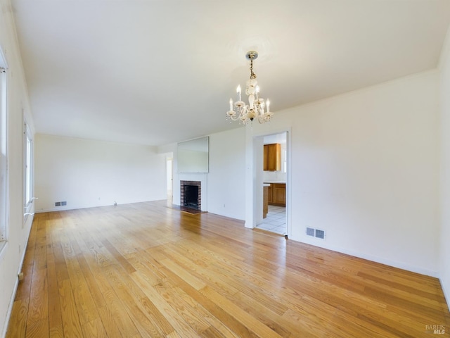 unfurnished living room featuring visible vents, a brick fireplace, a chandelier, and light wood finished floors