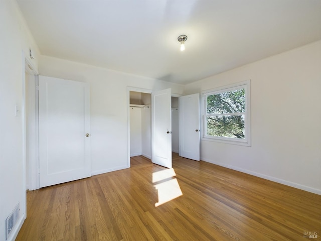 unfurnished bedroom featuring a closet, visible vents, baseboards, and wood finished floors