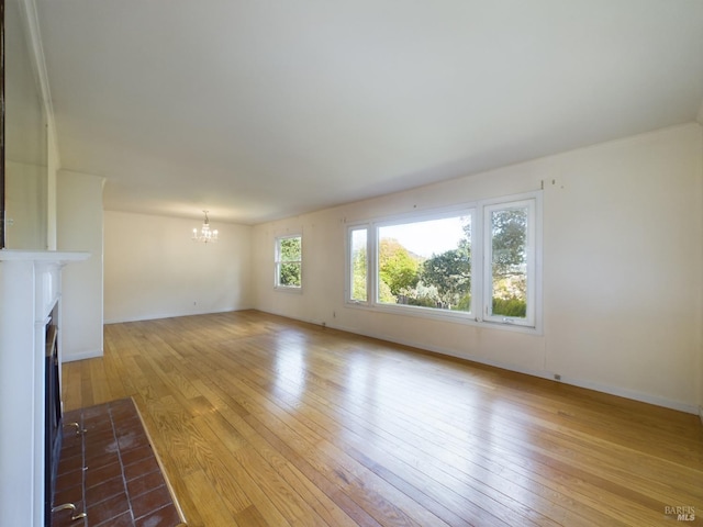 unfurnished living room featuring a notable chandelier, baseboards, a fireplace with flush hearth, and hardwood / wood-style floors