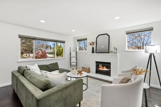 living area featuring dark wood-type flooring, a brick fireplace, a wealth of natural light, and baseboards