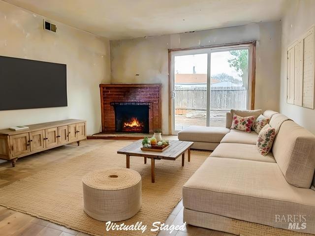 living room featuring light wood-type flooring, a brick fireplace, and visible vents