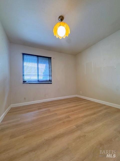 spare room featuring lofted ceiling, light wood finished floors, and baseboards