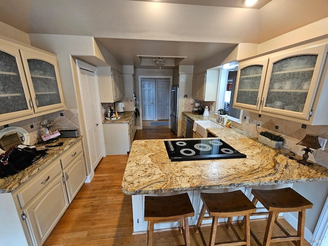 kitchen with a breakfast bar area, a sink, freestanding refrigerator, a peninsula, and wood finished floors