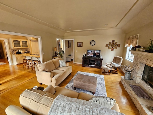 living room with baseboards, light wood-style flooring, and a stone fireplace