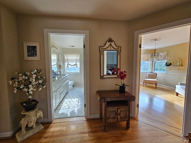 hallway featuring baseboards, a notable chandelier, a sink, and light wood-type flooring