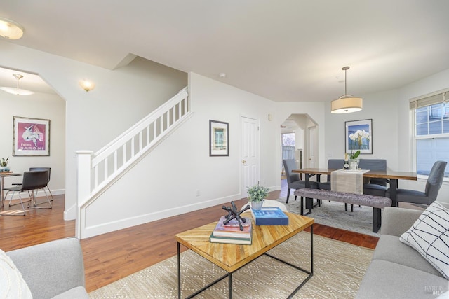 living area featuring arched walkways, stairway, baseboards, and wood finished floors