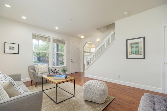 living area featuring wood finished floors, recessed lighting, arched walkways, baseboards, and stairs