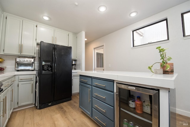 kitchen with wine cooler, black fridge with ice dispenser, light wood-type flooring, and light countertops