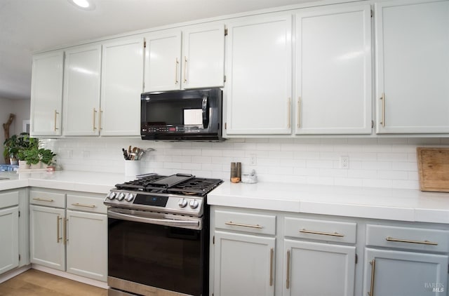 kitchen featuring tasteful backsplash, black microwave, light countertops, gas stove, and white cabinetry