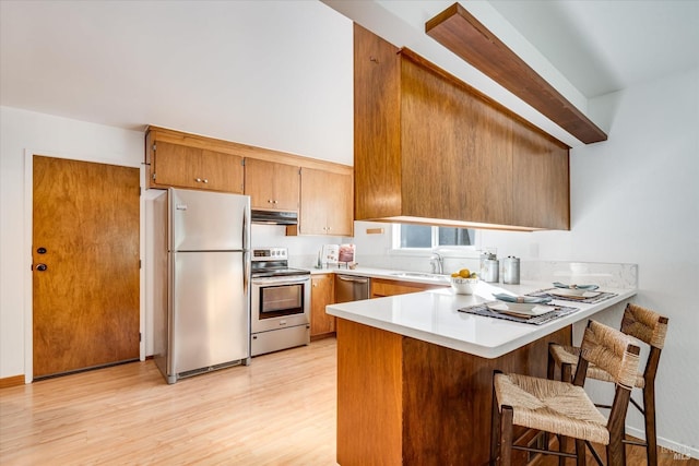 kitchen featuring light wood-style flooring, appliances with stainless steel finishes, a peninsula, light countertops, and under cabinet range hood