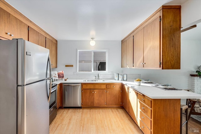 kitchen with a peninsula, a kitchen breakfast bar, light countertops, appliances with stainless steel finishes, and light wood-type flooring