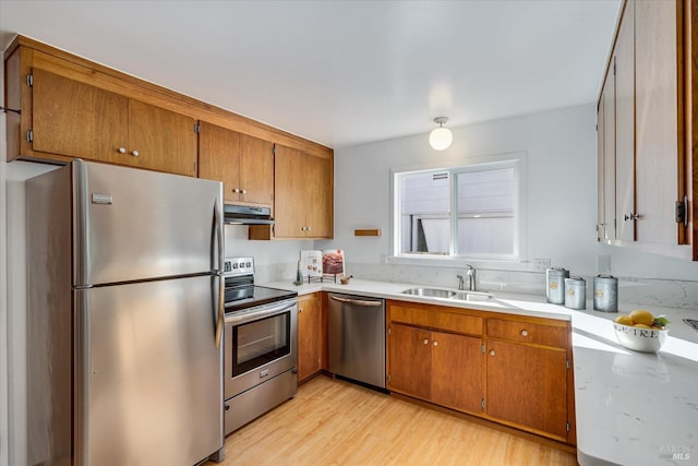 kitchen featuring stainless steel appliances, brown cabinetry, a sink, and under cabinet range hood