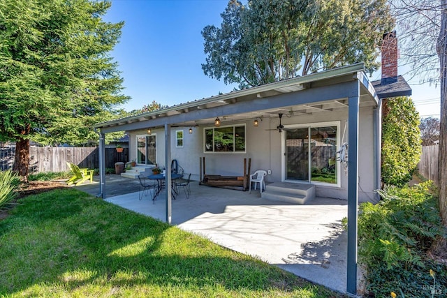 rear view of house featuring entry steps, fence, a yard, stucco siding, and a chimney