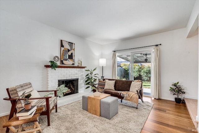 living room with a brick fireplace, baseboards, and wood finished floors