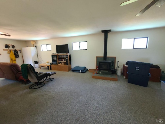 carpeted living area featuring a wood stove and a ceiling fan