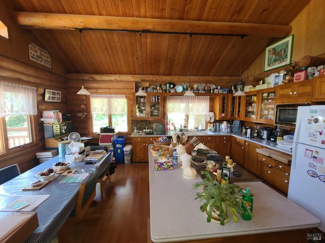 kitchen featuring brown cabinetry, dark wood finished floors, lofted ceiling with beams, stainless steel microwave, and freestanding refrigerator